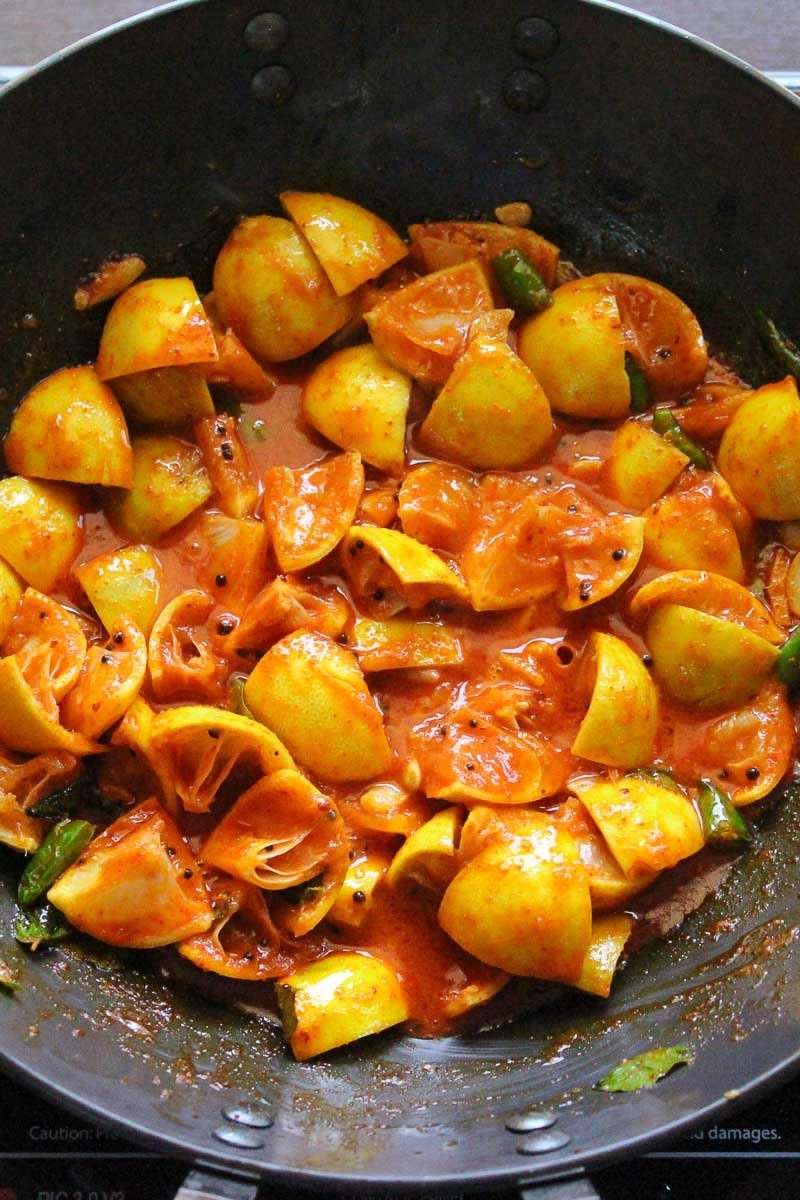 Lemon pickle cooking in a black kadai with red chilli, mustard seeds and green chillies