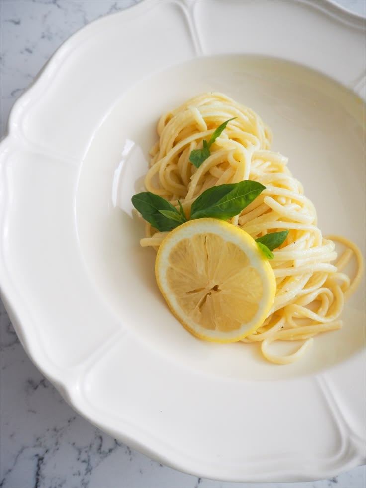 A nest of lemon pasta with basil and a lemon slice in a white scalloped bowl