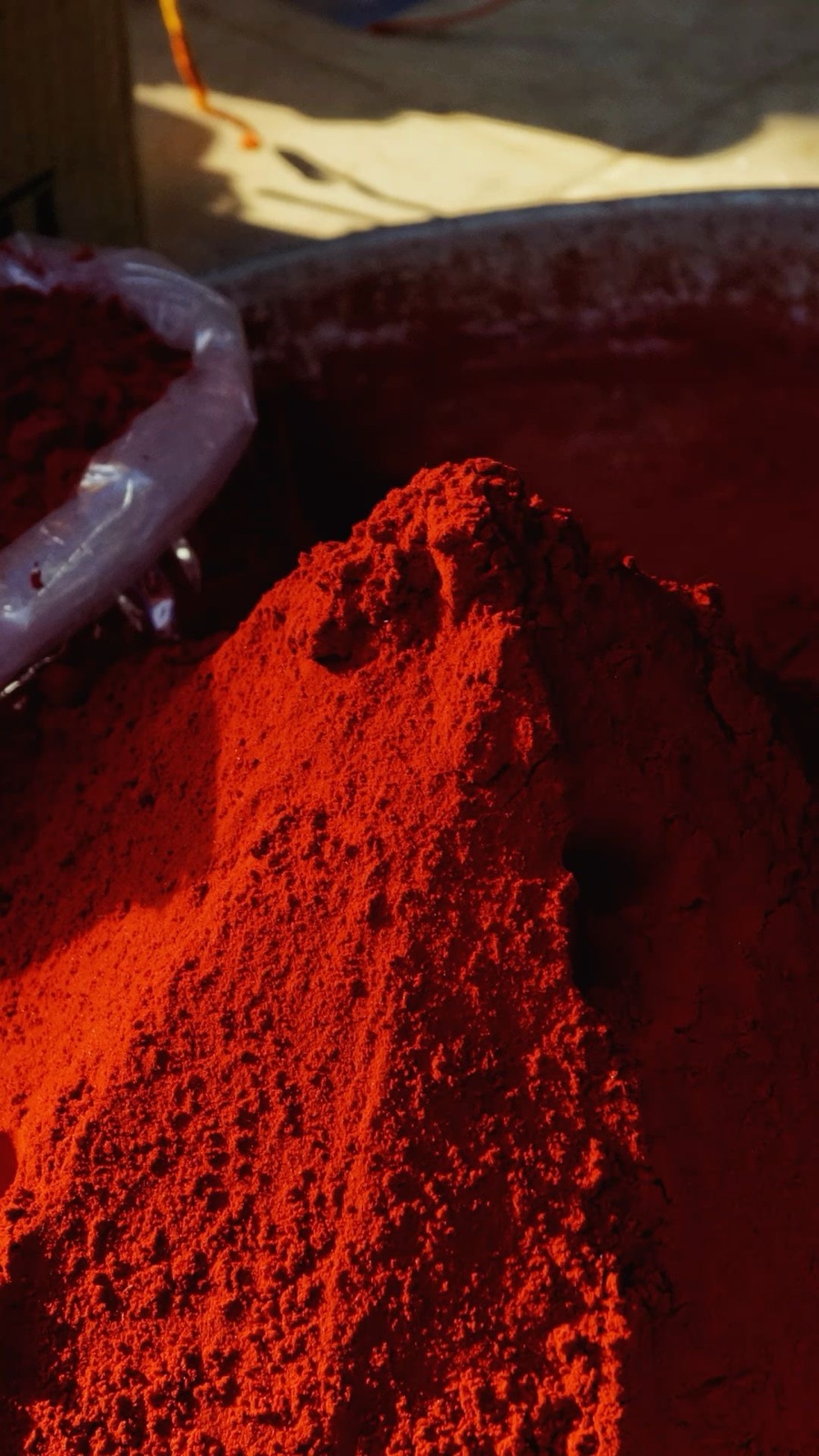 A heap of vermilion-red powder in a market vessel, lit by low sun